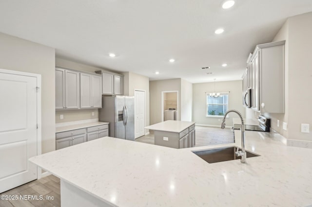 kitchen featuring sink, light stone counters, appliances with stainless steel finishes, a kitchen island, and washer / dryer