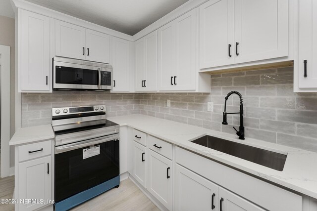 kitchen with decorative backsplash, white cabinetry, sink, and appliances with stainless steel finishes