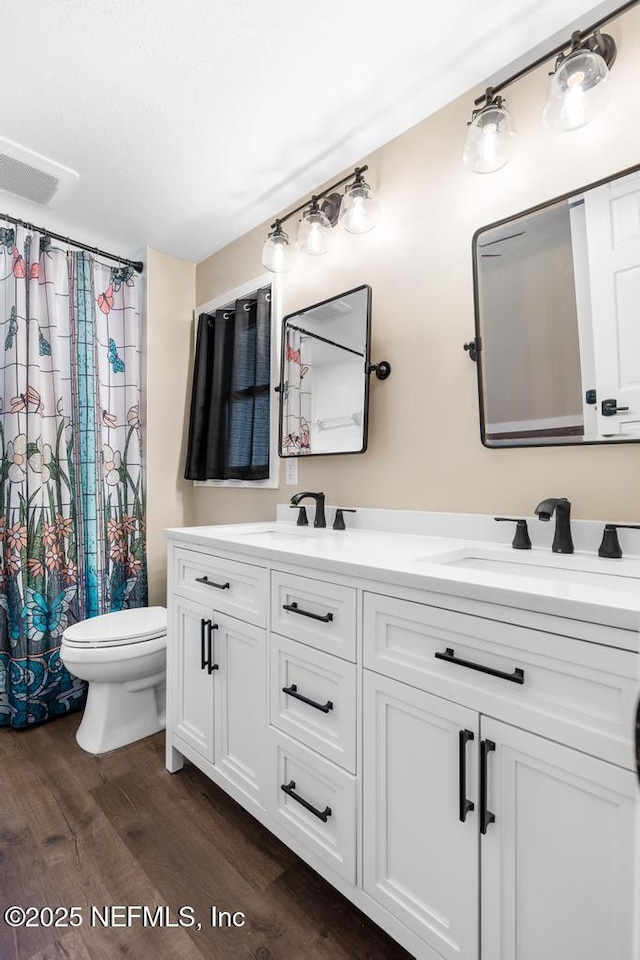 full bathroom featuring toilet, double vanity, a sink, and wood finished floors