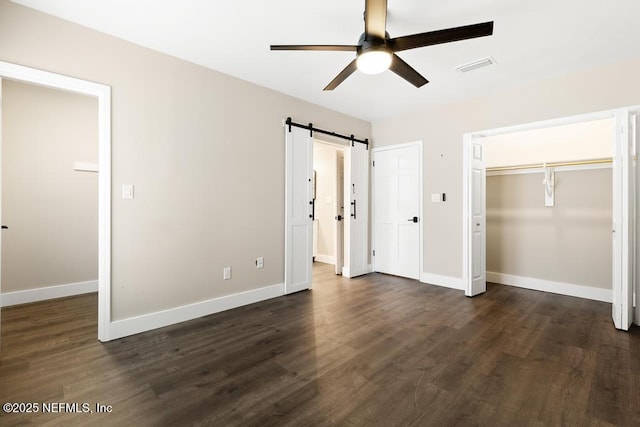 unfurnished bedroom with a barn door, dark wood-type flooring, visible vents, multiple closets, and baseboards