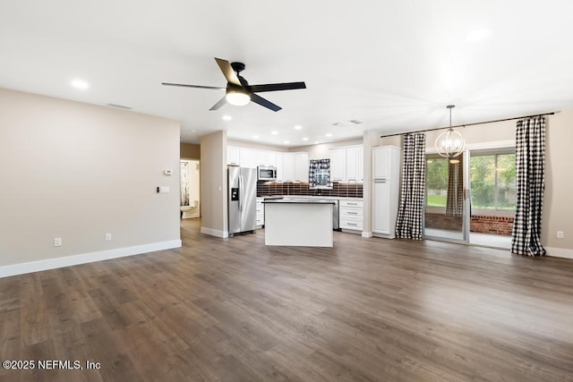 unfurnished living room with ceiling fan with notable chandelier, recessed lighting, dark wood finished floors, and baseboards