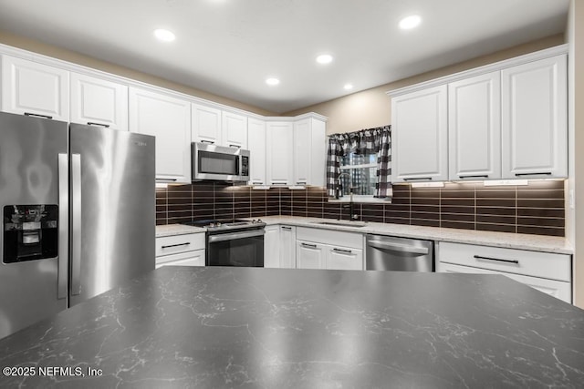 kitchen with tasteful backsplash, white cabinets, dark stone countertops, stainless steel appliances, and a sink