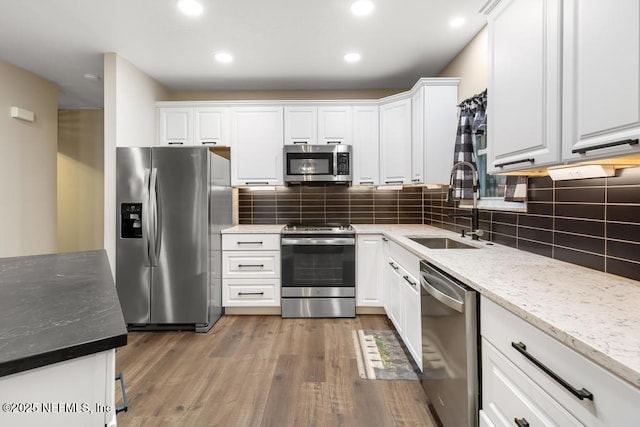 kitchen featuring stainless steel appliances, wood finished floors, a sink, and white cabinetry