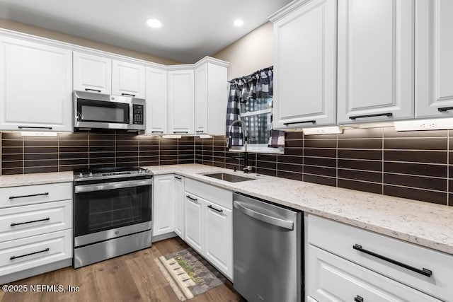 kitchen featuring stainless steel appliances, wood finished floors, a sink, white cabinetry, and decorative backsplash