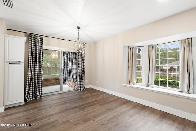 unfurnished dining area with a notable chandelier, baseboards, visible vents, and wood finished floors