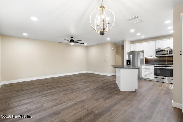 kitchen with white cabinets, appliances with stainless steel finishes, backsplash, dark countertops, and dark wood finished floors