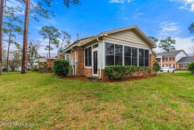 view of side of property featuring a yard, brick siding, and a sunroom