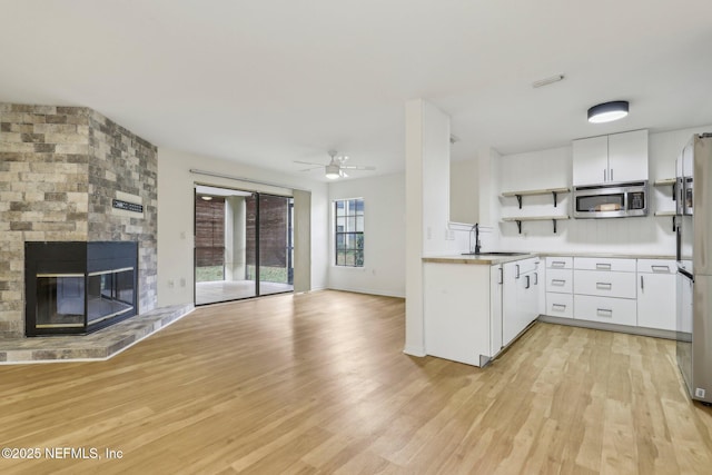 kitchen with ceiling fan, sink, light hardwood / wood-style flooring, a fireplace, and white cabinets