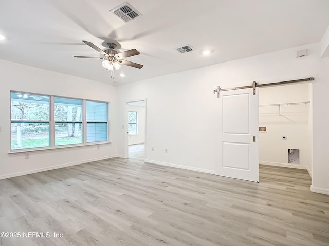 spare room with ceiling fan, a barn door, and light hardwood / wood-style floors