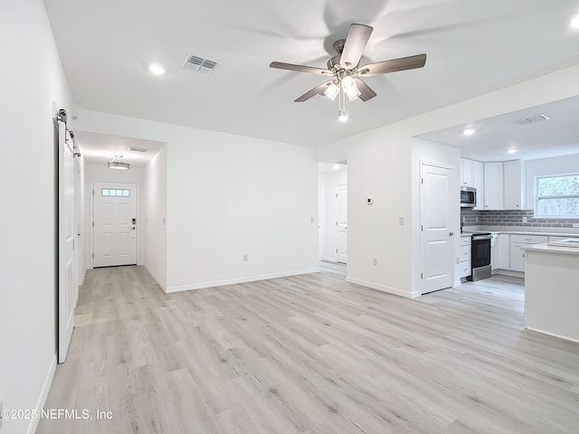 unfurnished living room featuring a barn door, ceiling fan, and light hardwood / wood-style flooring