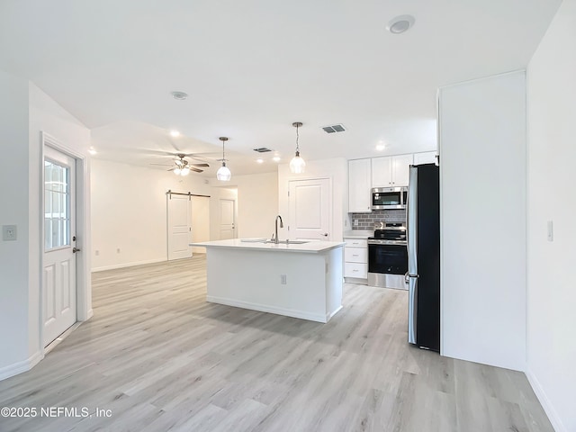 kitchen with white cabinetry, decorative backsplash, stainless steel appliances, a barn door, and a center island with sink