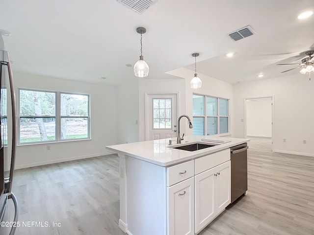 kitchen with appliances with stainless steel finishes, white cabinetry, sink, hanging light fixtures, and a center island with sink