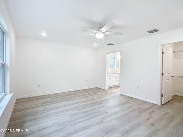 unfurnished bedroom featuring ensuite bathroom, a walk in closet, ceiling fan, light hardwood / wood-style floors, and a closet