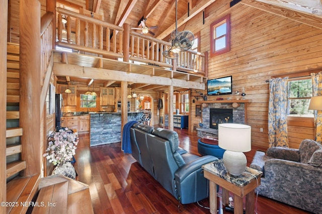 living room featuring dark wood-type flooring, ceiling fan, wooden walls, high vaulted ceiling, and a stone fireplace