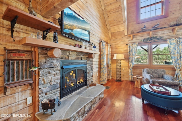 living room with hardwood / wood-style flooring, a stone fireplace, high vaulted ceiling, and wood walls