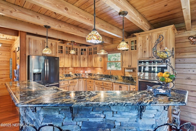 kitchen featuring dark stone countertops, decorative light fixtures, wooden walls, and appliances with stainless steel finishes