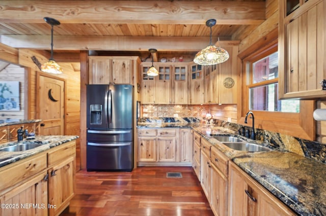 kitchen featuring stainless steel refrigerator with ice dispenser, dark stone counters, sink, and hanging light fixtures