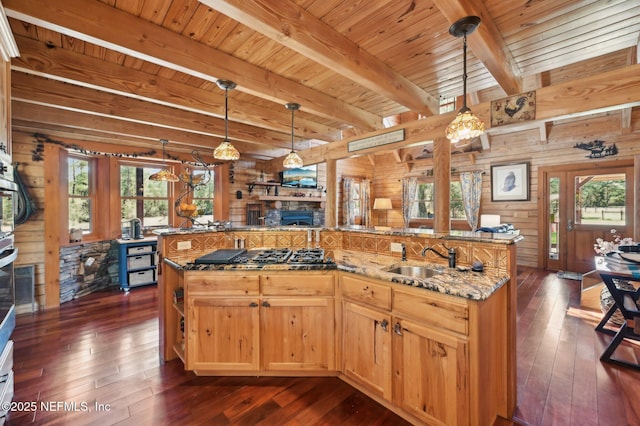 kitchen with sink, wood walls, light stone counters, dark hardwood / wood-style flooring, and pendant lighting