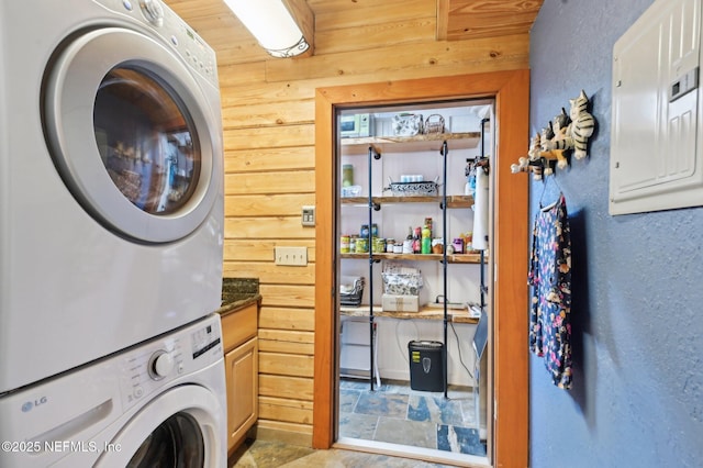 washroom with stacked washer / dryer, wooden walls, electric panel, and cabinets