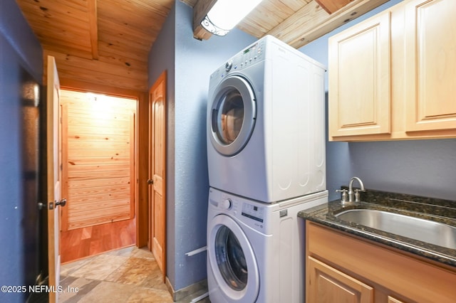 laundry area featuring cabinets, stacked washer / drying machine, sink, and wood ceiling