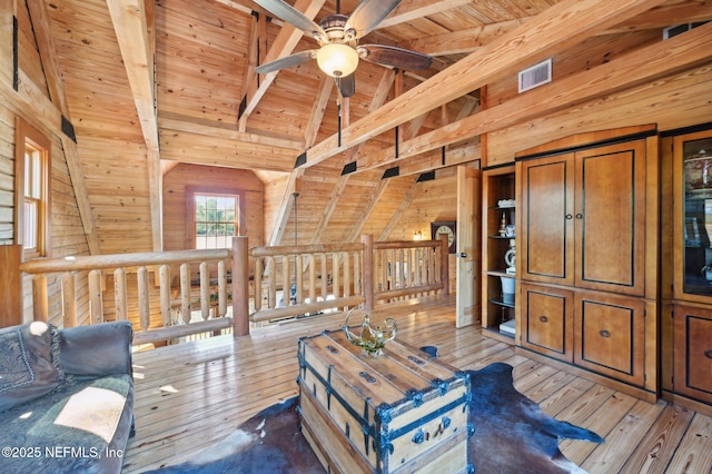 living area featuring wood walls, vaulted ceiling with beams, wooden ceiling, light wood-type flooring, and ceiling fan