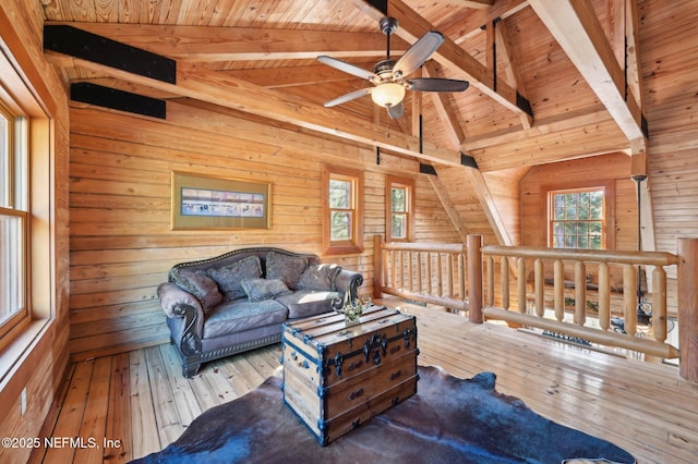 living room with vaulted ceiling with beams, wood ceiling, light wood-type flooring, wooden walls, and ceiling fan