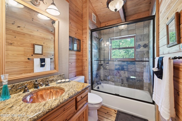 full bathroom with combined bath / shower with glass door, wood walls, vanity, toilet, and wooden ceiling