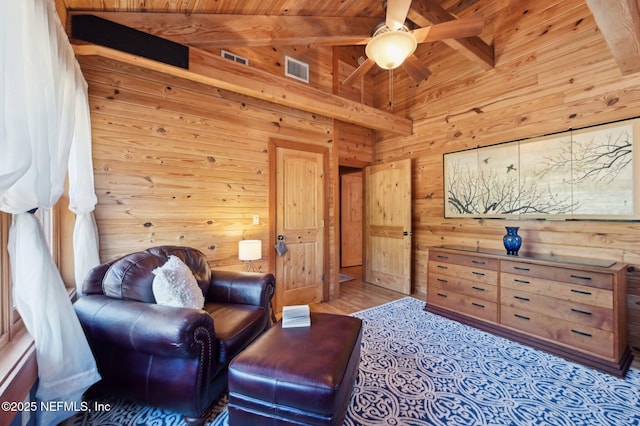 sitting room with wood ceiling, ceiling fan, vaulted ceiling with beams, wooden walls, and light hardwood / wood-style floors