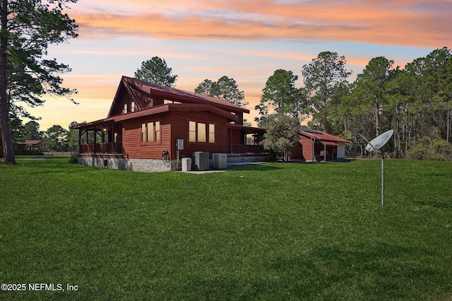 back house at dusk featuring central AC and a lawn