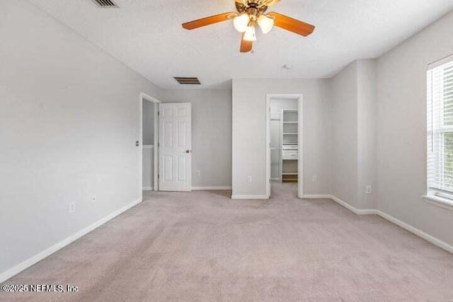 unfurnished bedroom featuring light carpet, a textured ceiling, a spacious closet, and ceiling fan