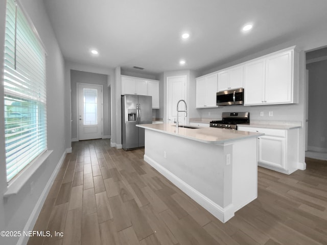 kitchen featuring stainless steel appliances, white cabinetry, sink, and an island with sink