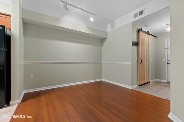 empty room featuring light wood-type flooring, a barn door, rail lighting, and ornamental molding