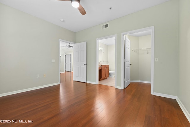 unfurnished bedroom with ensuite bathroom, ceiling fan, wood-type flooring, a spacious closet, and a closet