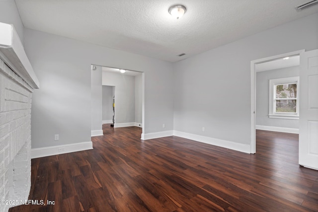 spare room with a textured ceiling, dark hardwood / wood-style floors, and a brick fireplace