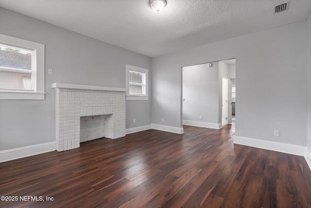 unfurnished living room with dark hardwood / wood-style flooring, a textured ceiling, and a brick fireplace