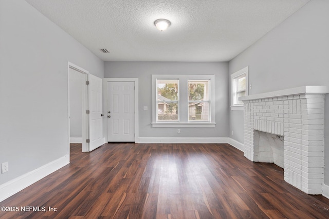 unfurnished living room featuring dark hardwood / wood-style floors, a textured ceiling, and a brick fireplace