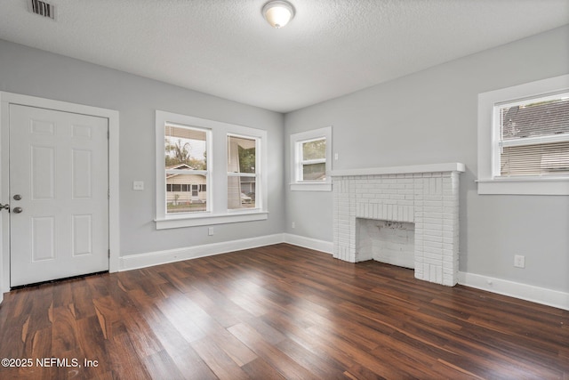 unfurnished living room with dark hardwood / wood-style flooring, a textured ceiling, and a brick fireplace