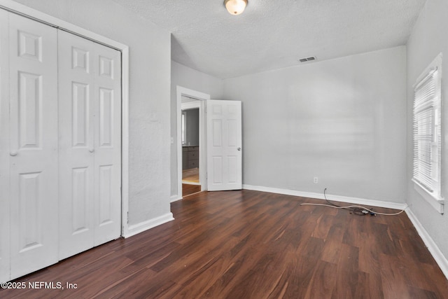 unfurnished bedroom with a textured ceiling, dark hardwood / wood-style flooring, and a closet