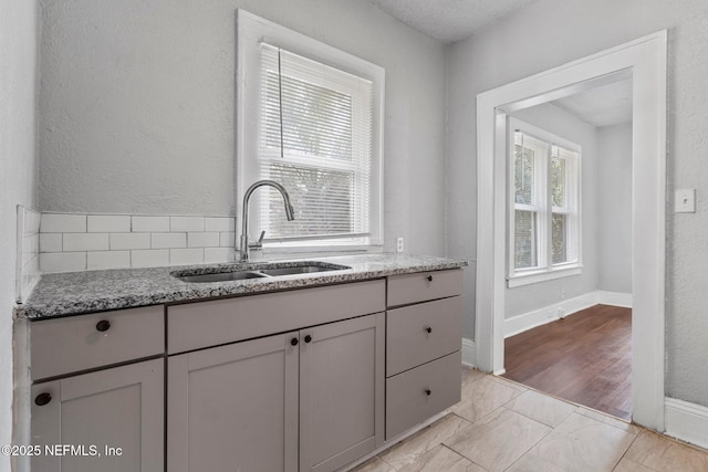 kitchen with gray cabinets, light stone counters, and sink