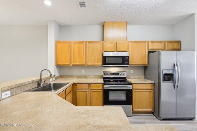 kitchen with stainless steel appliances, light hardwood / wood-style floors, sink, and a textured ceiling