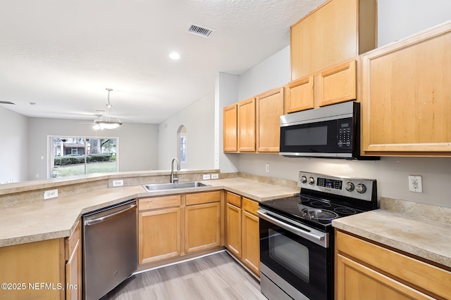 kitchen with sink, light brown cabinets, appliances with stainless steel finishes, kitchen peninsula, and light hardwood / wood-style floors