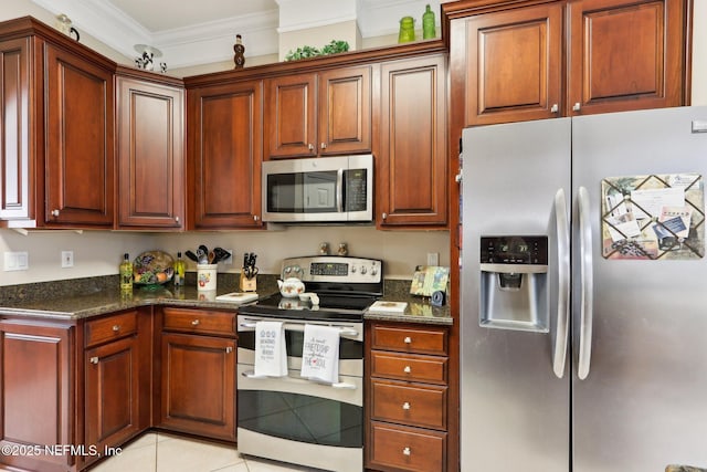 kitchen with dark stone countertops, ornamental molding, stainless steel appliances, and light tile patterned floors