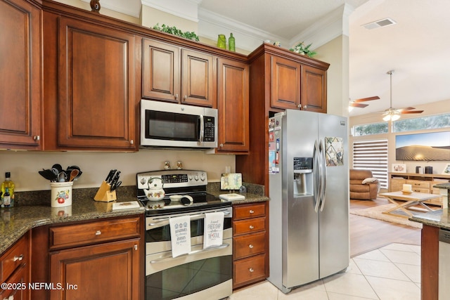 kitchen with dark stone counters, ornamental molding, light tile patterned floors, ceiling fan, and stainless steel appliances