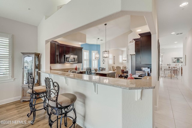 kitchen featuring kitchen peninsula, a kitchen breakfast bar, light stone countertops, vaulted ceiling, and decorative light fixtures