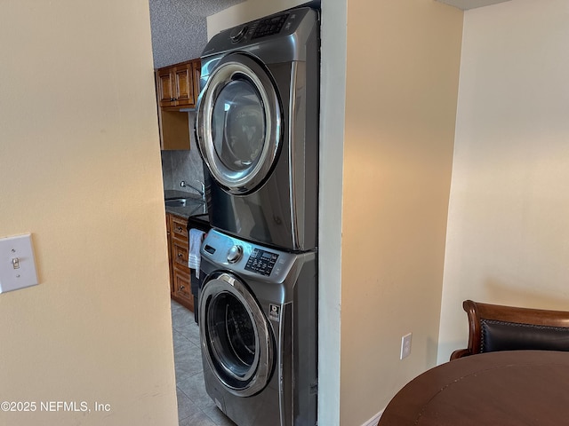 clothes washing area featuring stacked washer and dryer, a textured ceiling, and sink