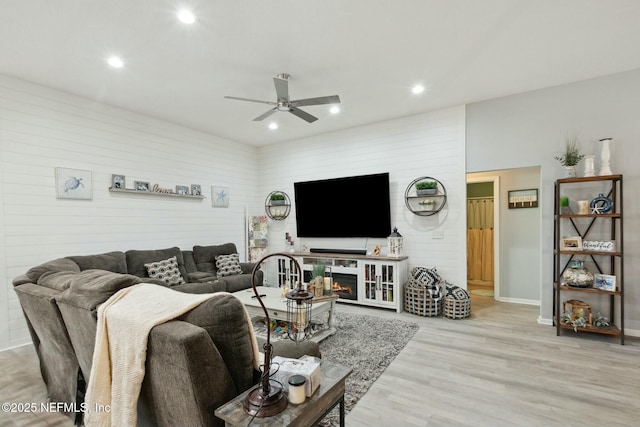 living room with wooden walls, ceiling fan, and light wood-type flooring