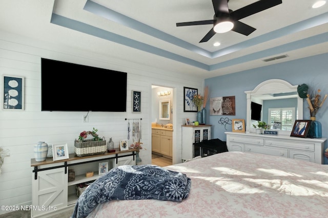 bedroom with ceiling fan, a raised ceiling, wooden walls, and ensuite bath