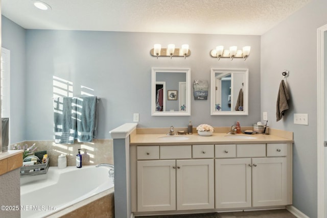 bathroom with vanity, a textured ceiling, and tiled tub