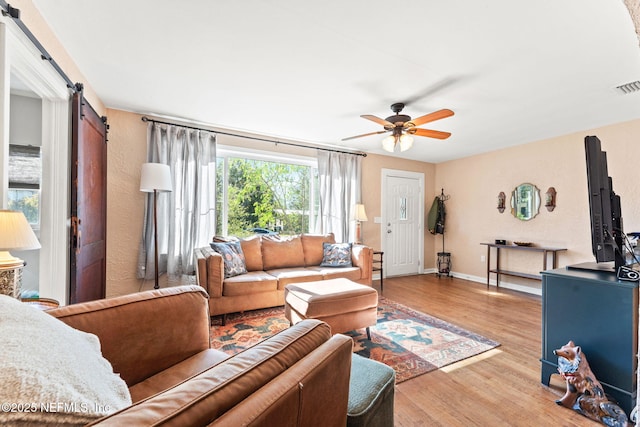 living room featuring hardwood / wood-style floors, ceiling fan, and a barn door