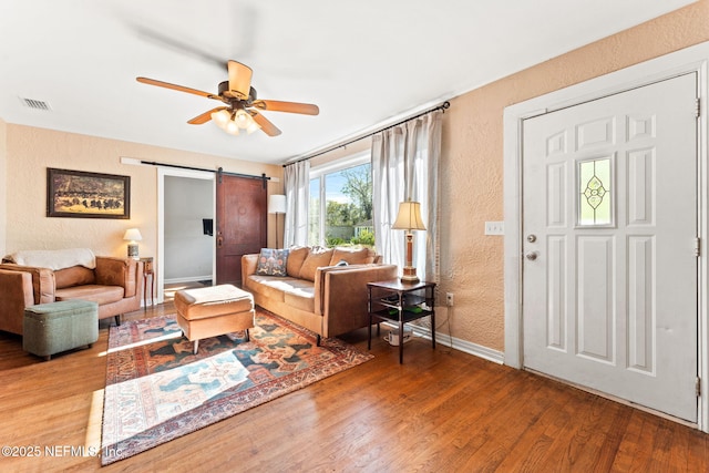 living room with hardwood / wood-style flooring, ceiling fan, and a barn door